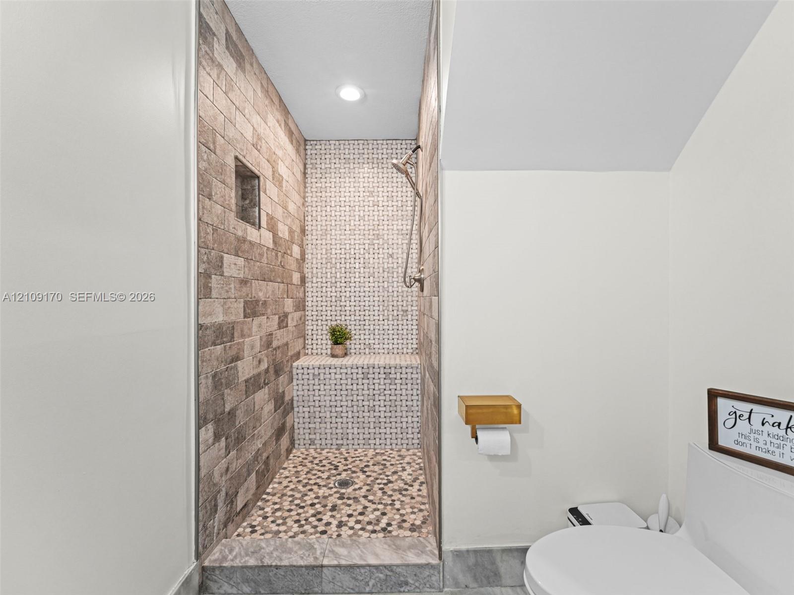 Walk-in shower featuring a brick-style tiled wall, mosaic-tile accents, built-in tiled bench, river-stone flooring, and a metal shower fixture