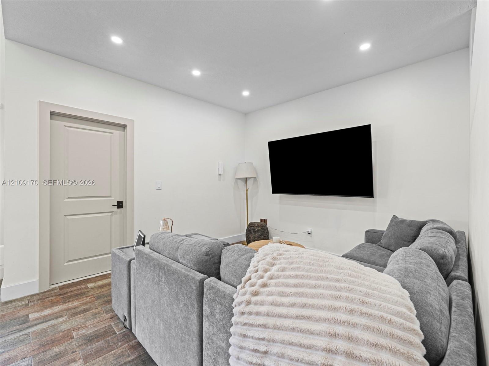 Interior room featuring wood-finish flooring, recessed lighting, and a multi-panel door with matte black hardware Interior room featuring wood-finish flooring, recessed lighting, and a multi-panel door with matte black hardware