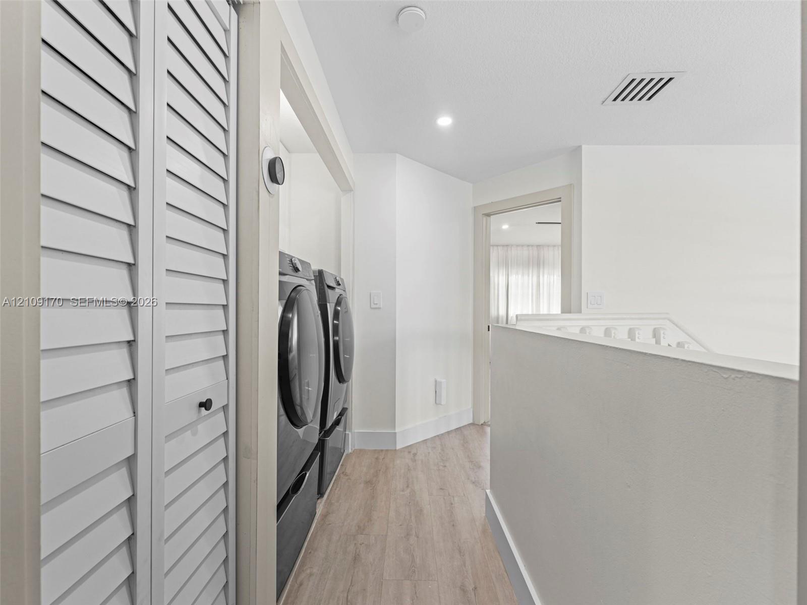 Laundry area featuring wood-finish flooring, white louvered closet doors, and recessed lighting