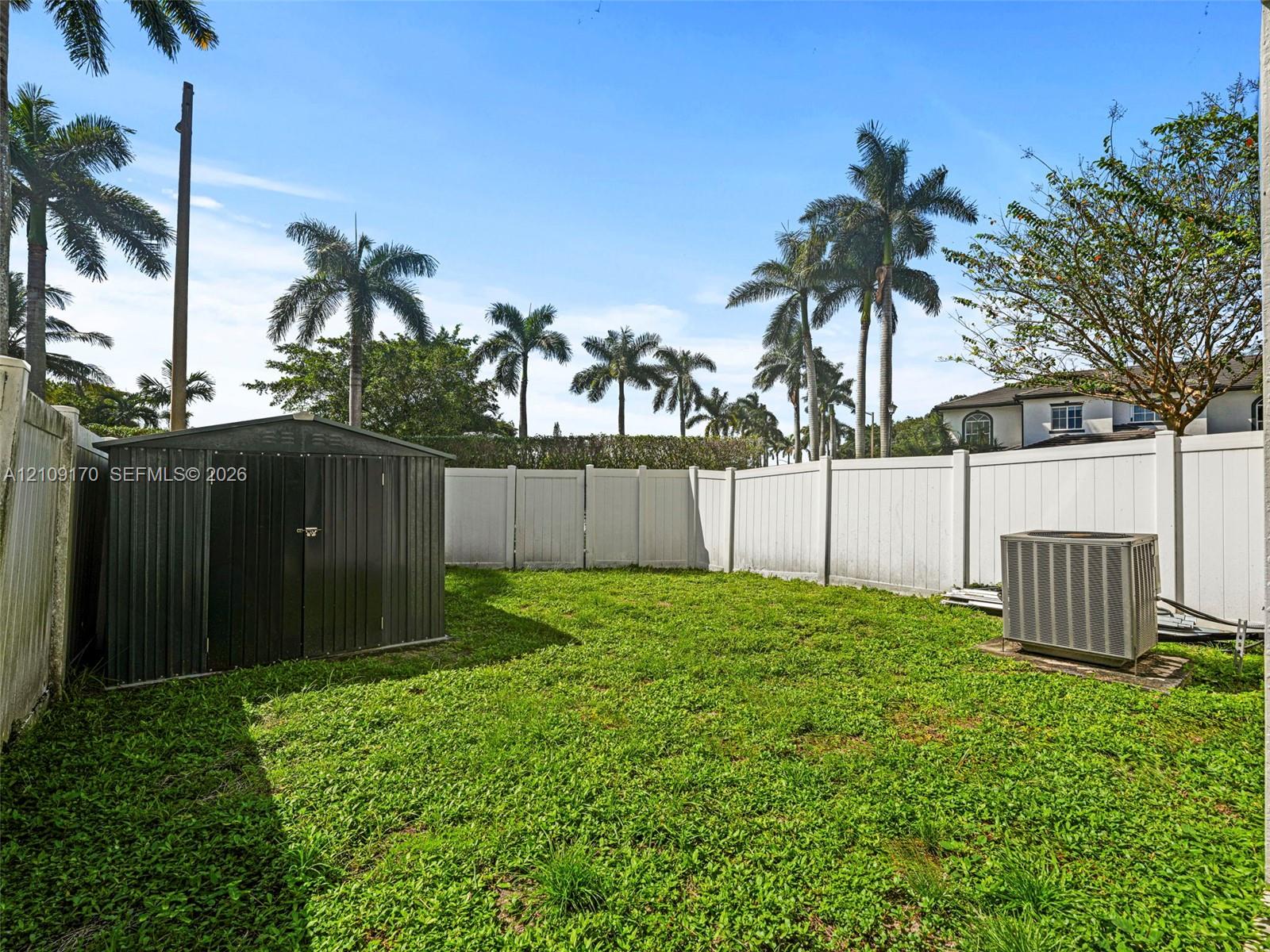 Fenced backyard featuring a manicured lawn, metal storage shed, and mature palm trees