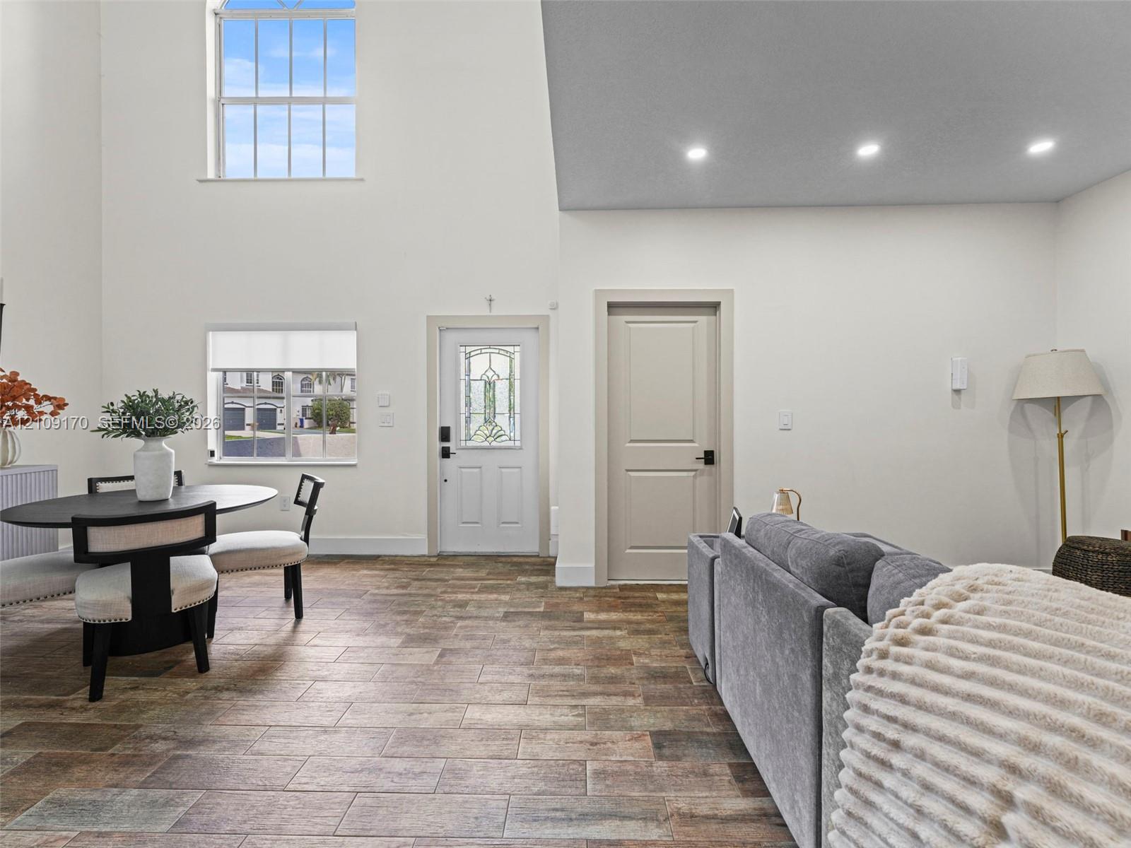 High-ceiling interior space featuring multi-tonal rectangular tile flooring, recessed lighting, double-hung windows, and a glass-inset entry door High-ceiling interior space featuring multi-tonal rectangular tile flooring, recessed lighting, double-hung windows, and a glass-inset entry door