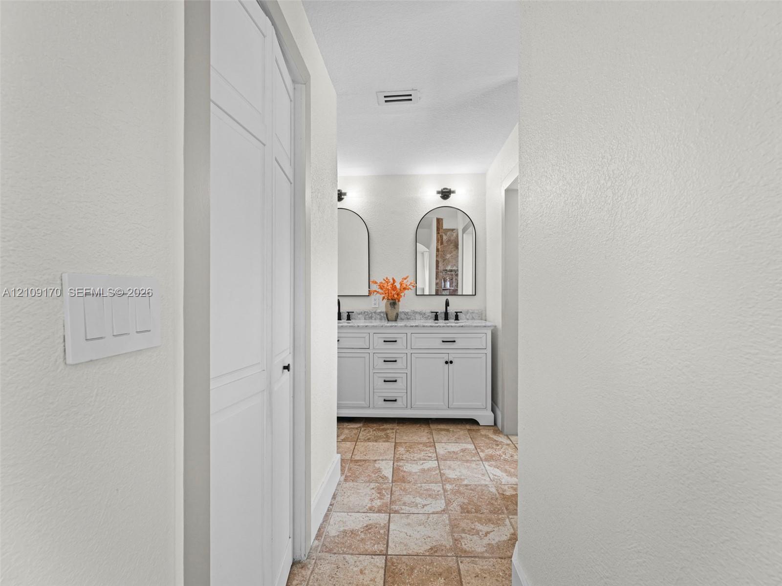 Dual-sink vanity with light-colored cabinetry, stone-finish countertops, arched mirrors, and tile flooring