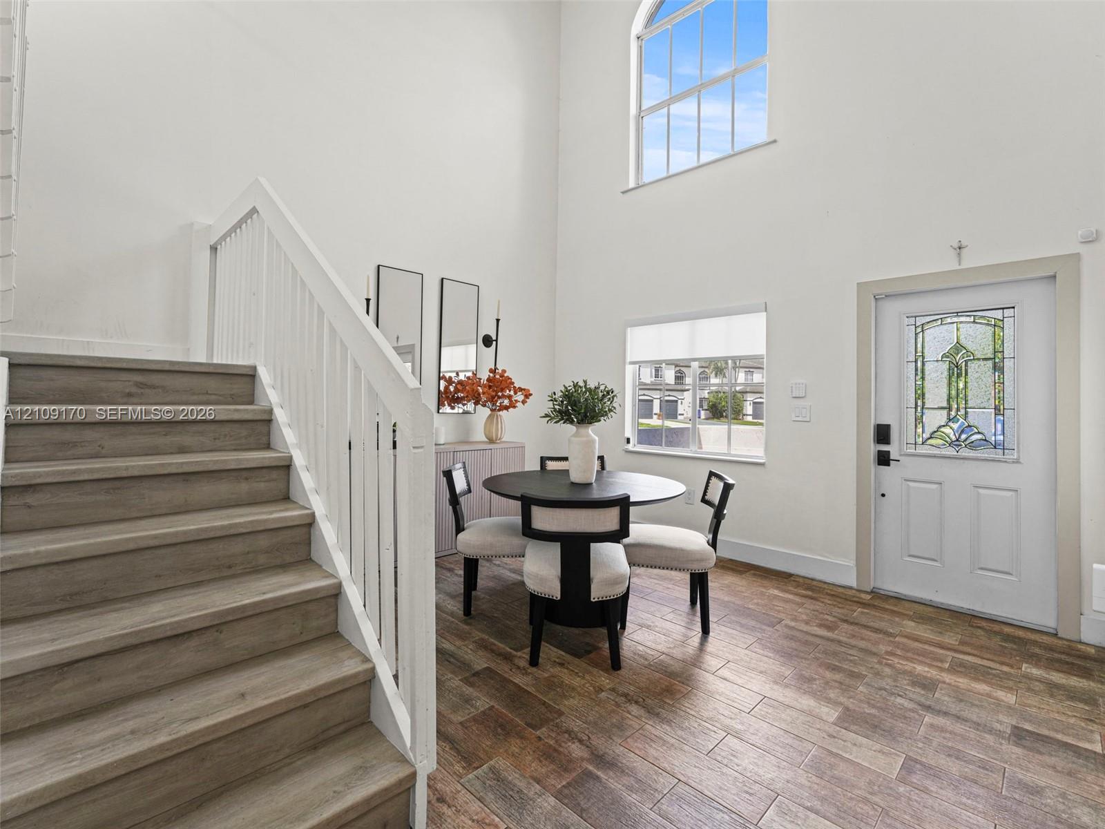 Double-height ceiling, arched window, wood-finish flooring, staircase with white railing, and exterior door with decorative glass inlay