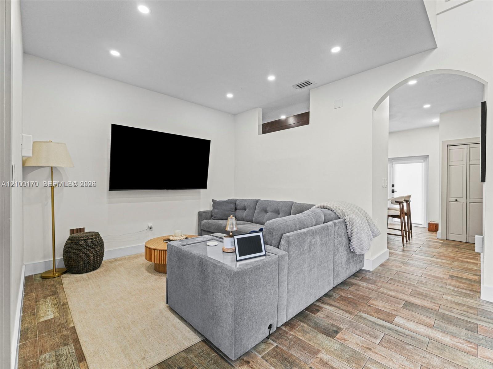 Living area featuring wood-finish tile flooring, recessed lighting, and a prominent arched entryway Living area featuring wood-finish tile flooring, recessed lighting, and a prominent arched entryway