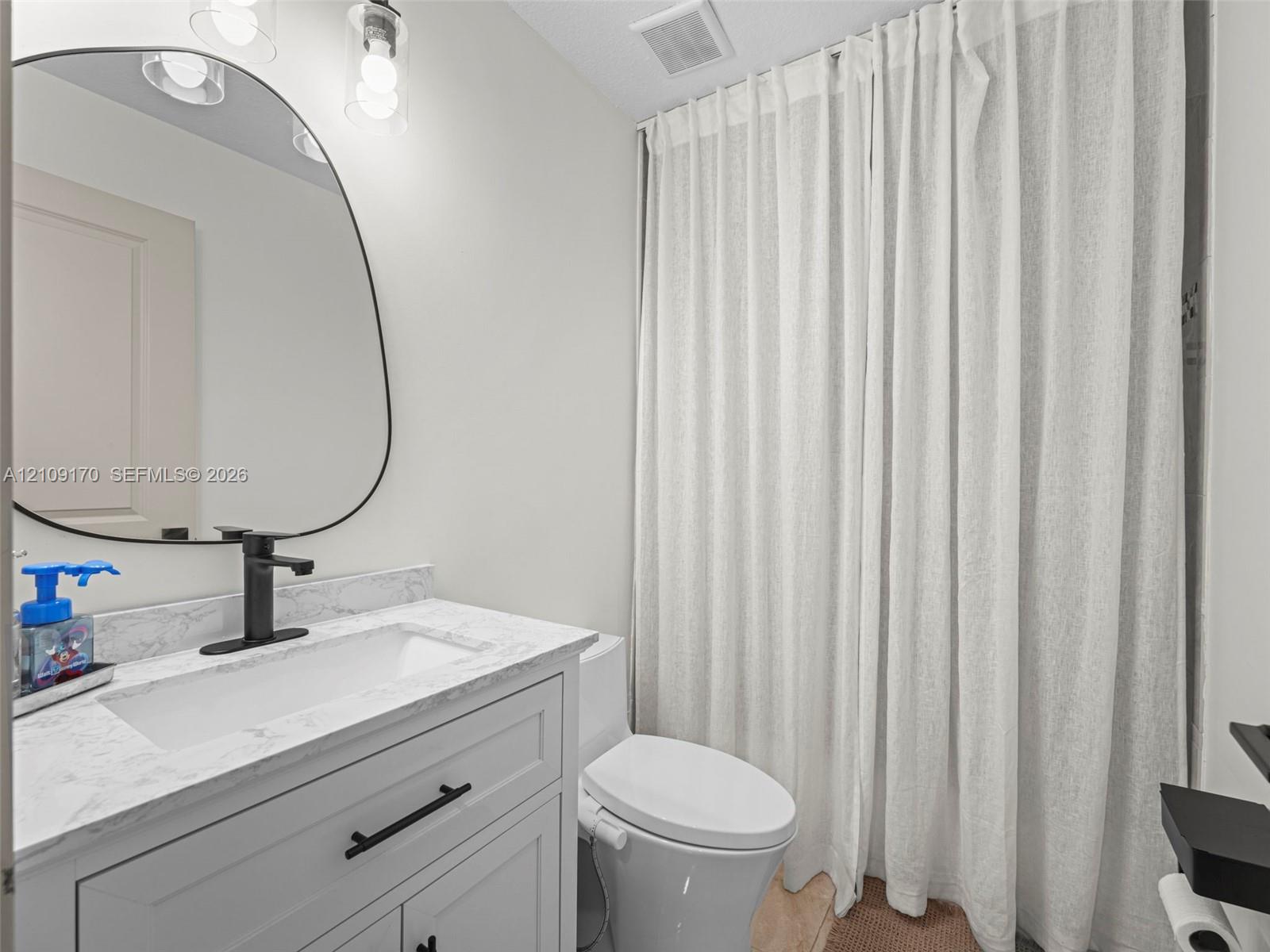Bathroom featuring a vanity with stone-finish countertop, undermount rectangular sink, matte black faucet, and an irregular-shaped mirror