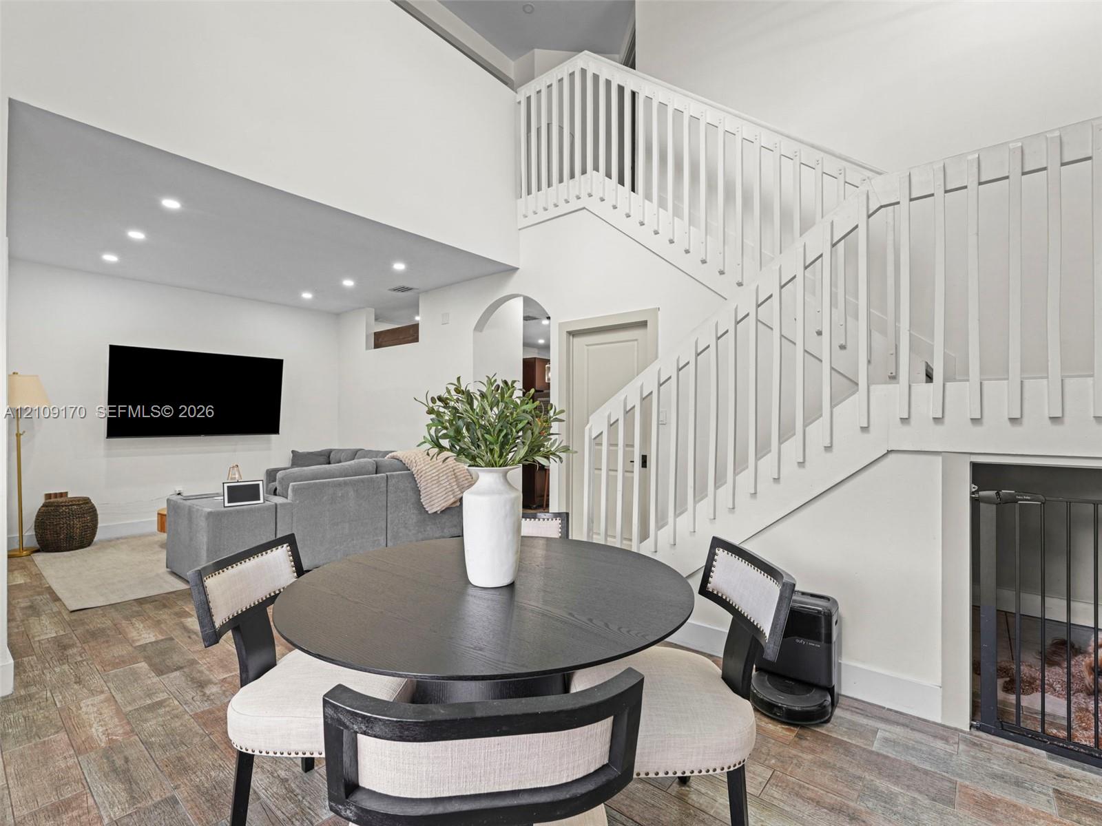 High-ceiling interior featuring a wooden staircase with vertical balusters, wood-finish flooring, recessed lighting, and an arched doorway High-ceiling interior featuring a wooden staircase with vertical balusters, wood-finish flooring, recessed lighting, and an arched doorway