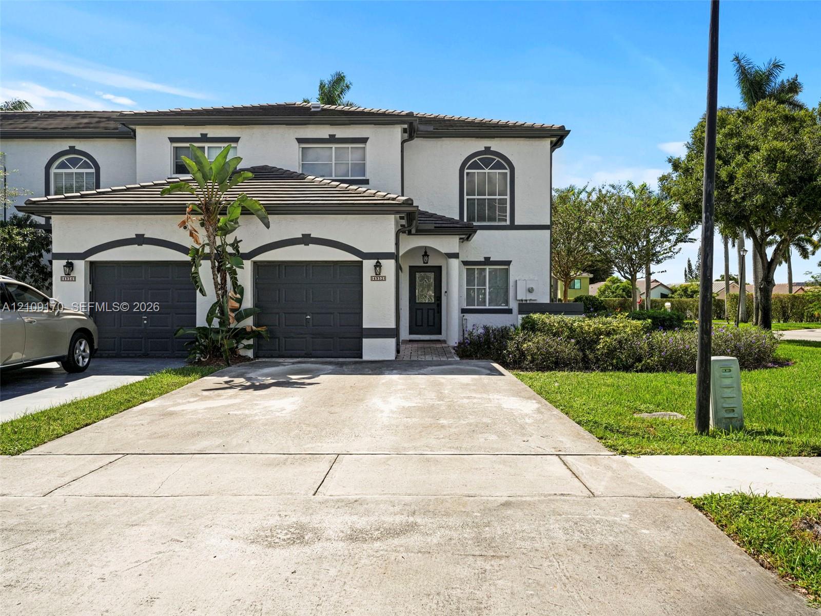 Stucco exterior featuring arched garage entryways, a tile roof, decorative trim detailing, and an attached two-car garage