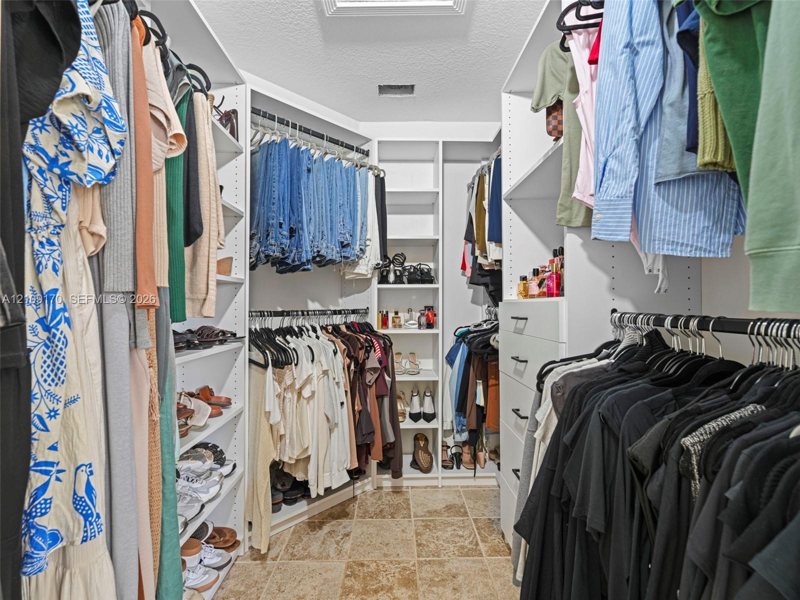 Walk-in closet featuring white built-in shelving, multiple hanging rods, integrated drawer storage, and tile flooring