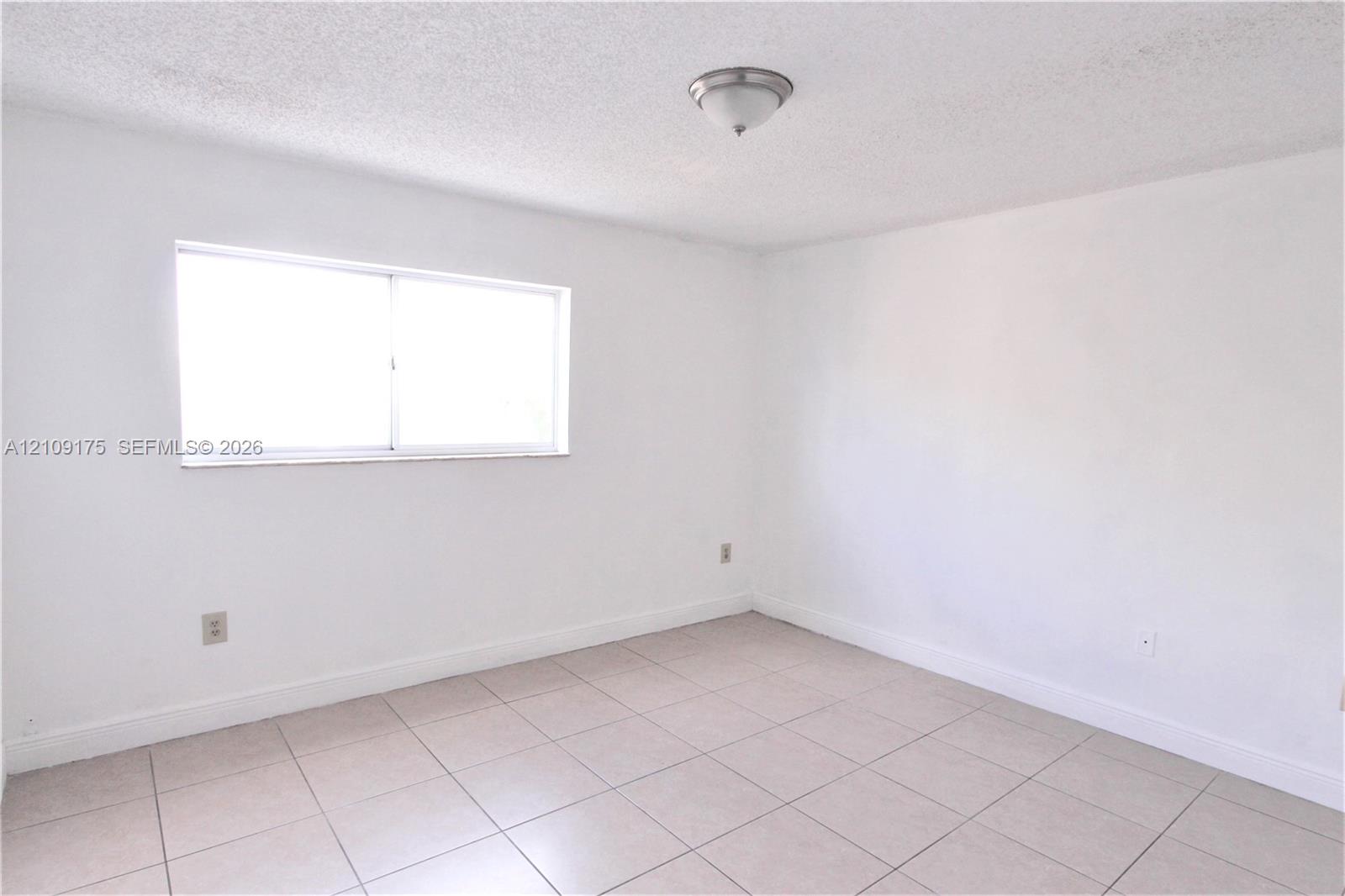 Room with large-format light-toned tile flooring, neutral wall finishes, single-pane sliding window, and ceiling-mounted dome light fixture