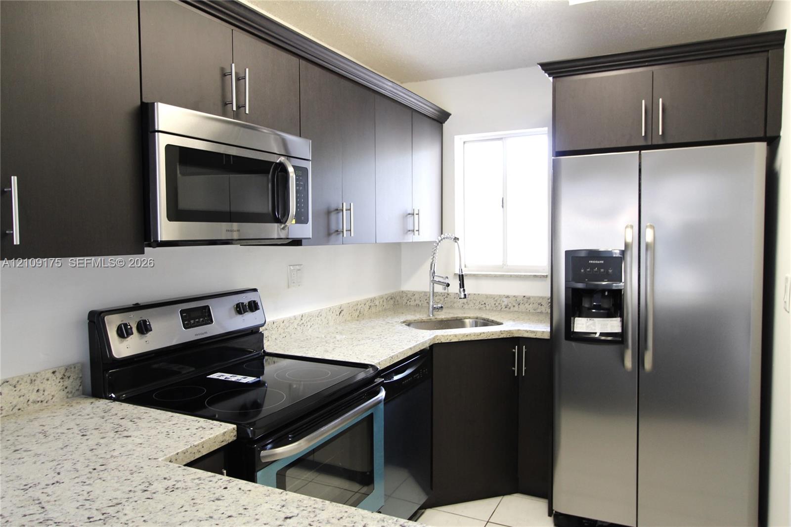 Kitchen featuring dark-toned cabinetry, stainless steel appliances, stone-patterned countertops, a stainless steel gooseneck faucet, and a dual-basin sink