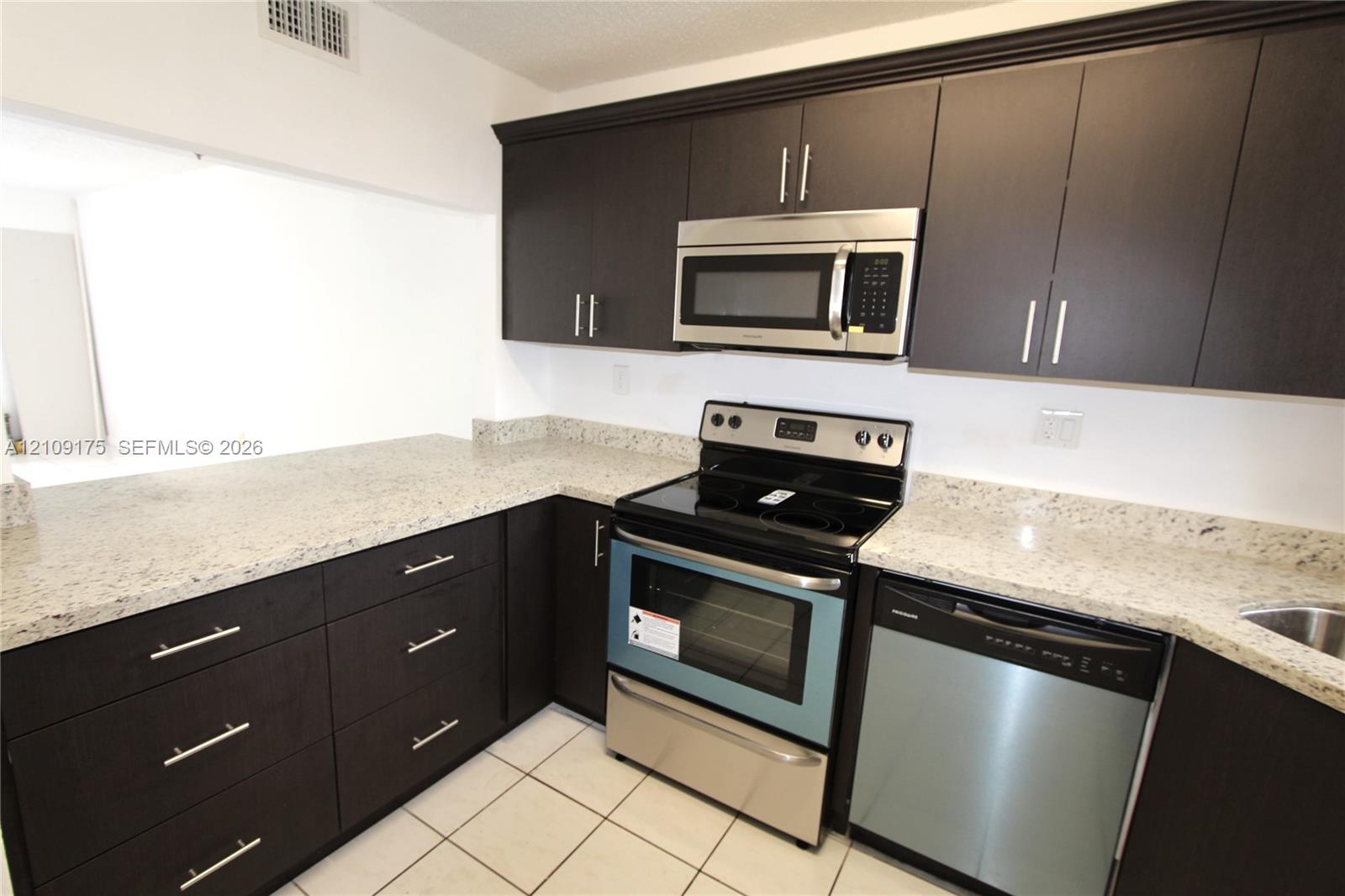 Kitchen featuring dark cabinetry, stone-finish countertops, stainless steel appliances, and ceramic tile flooring