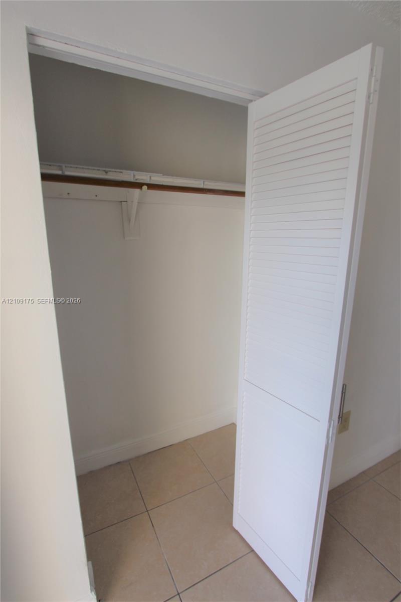 Storage closet featuring a white louvered door and a built-in shelf with a hanging rod