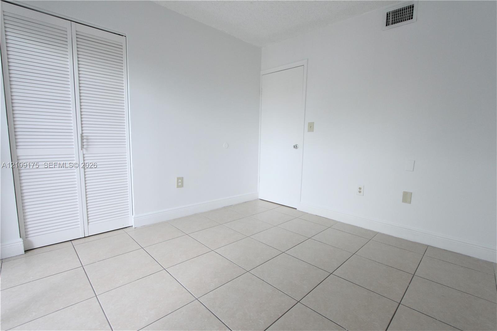 Neutral-toned tile flooring, white louvered-door closet, and solid core interior door