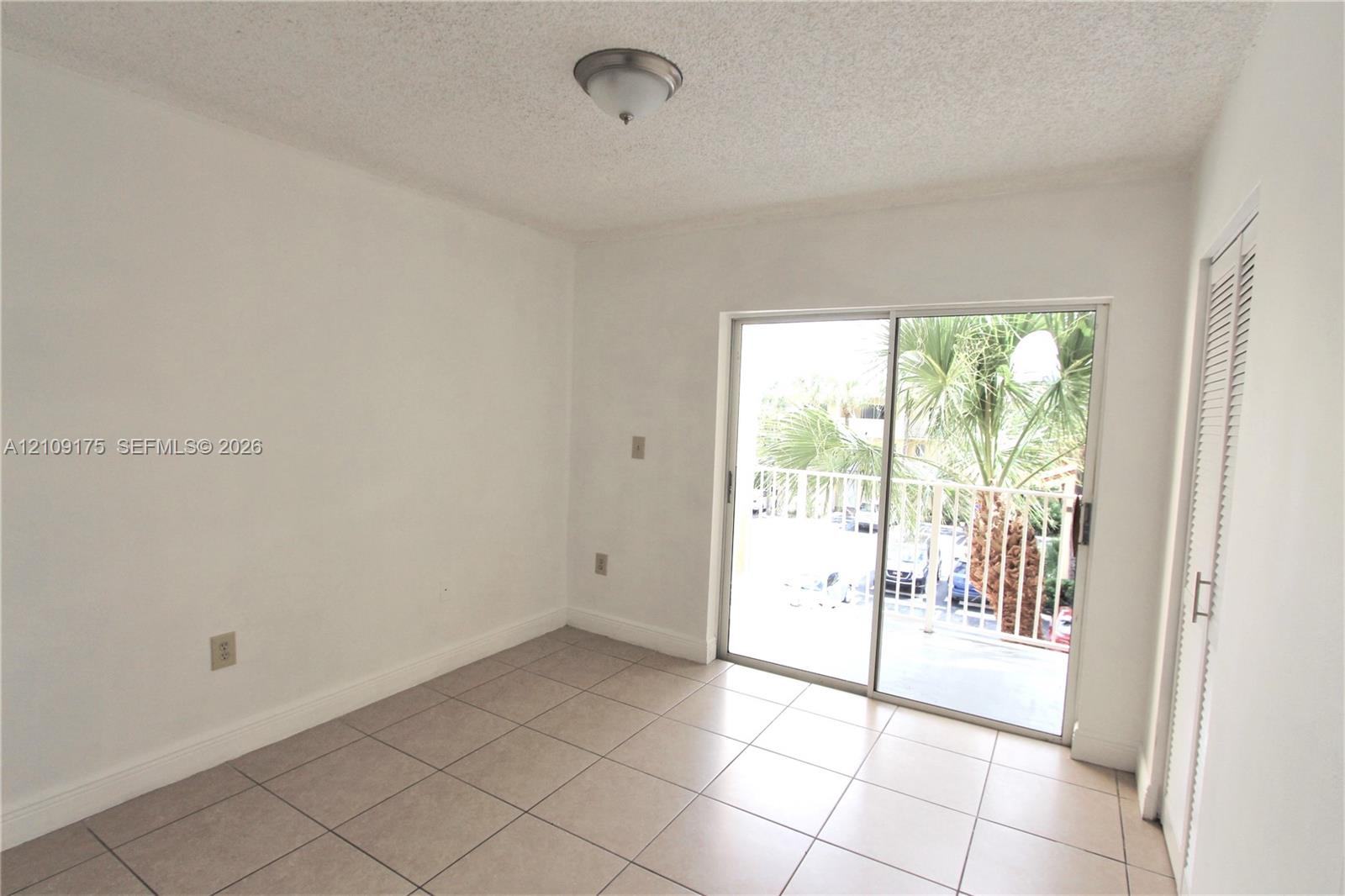 Interior space featuring neutral tile flooring, sliding glass doors, a balcony, and louvered-door closet cabinetry
