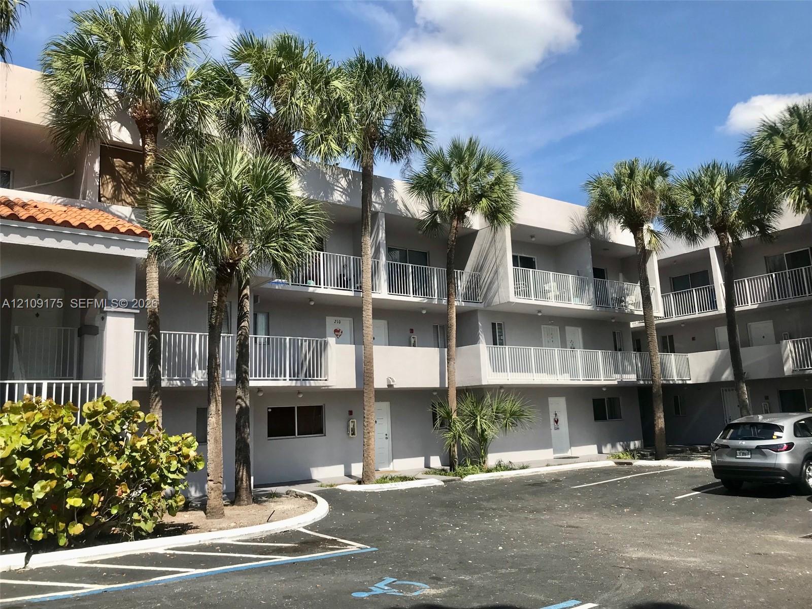 Multi-story exterior featuring a neutral stucco facade, private balconies with white railings, and mature palm landscaping