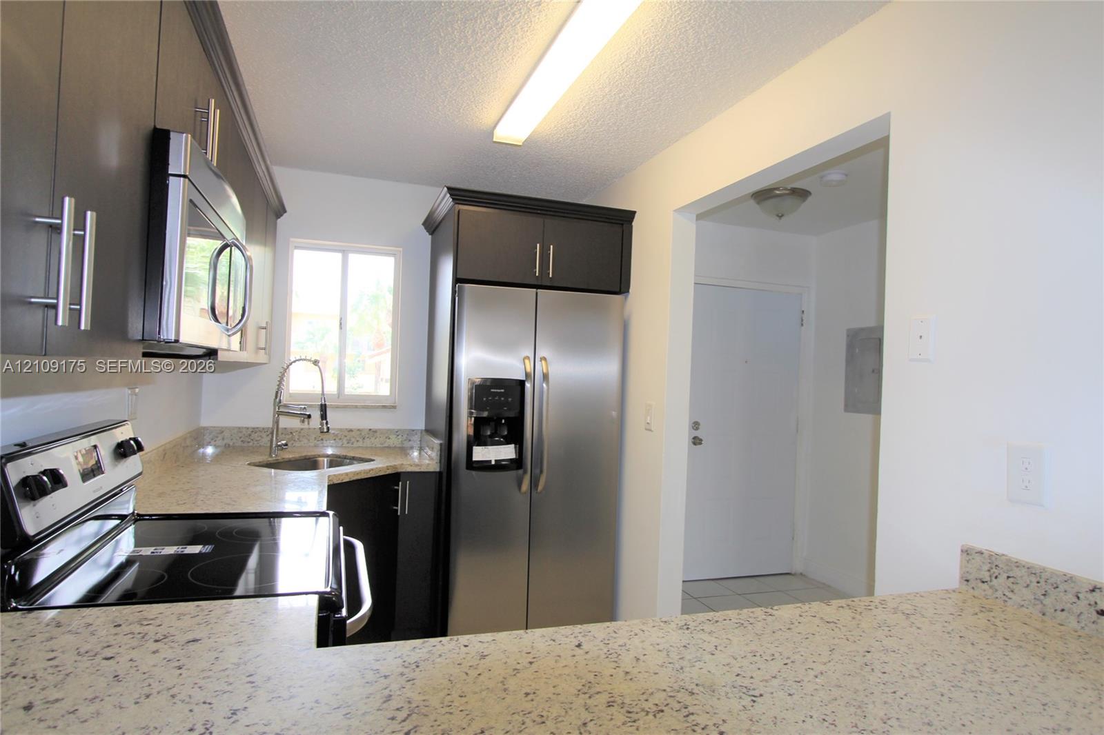 Kitchen featuring dark cabinetry, stone-finish countertops, stainless steel appliances, and a modern gooseneck faucet