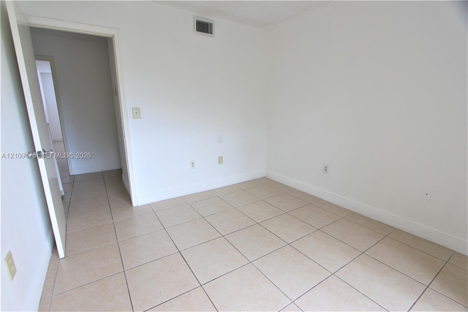 Neutral-toned ceramic tile flooring, clean white walls, and interior swing door