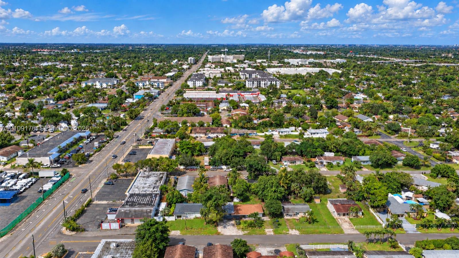 Aerial perspective of an urban setting featuring paved thoroughfares, established residential blocks, mature tree canopy, and access to commercial infrastructure