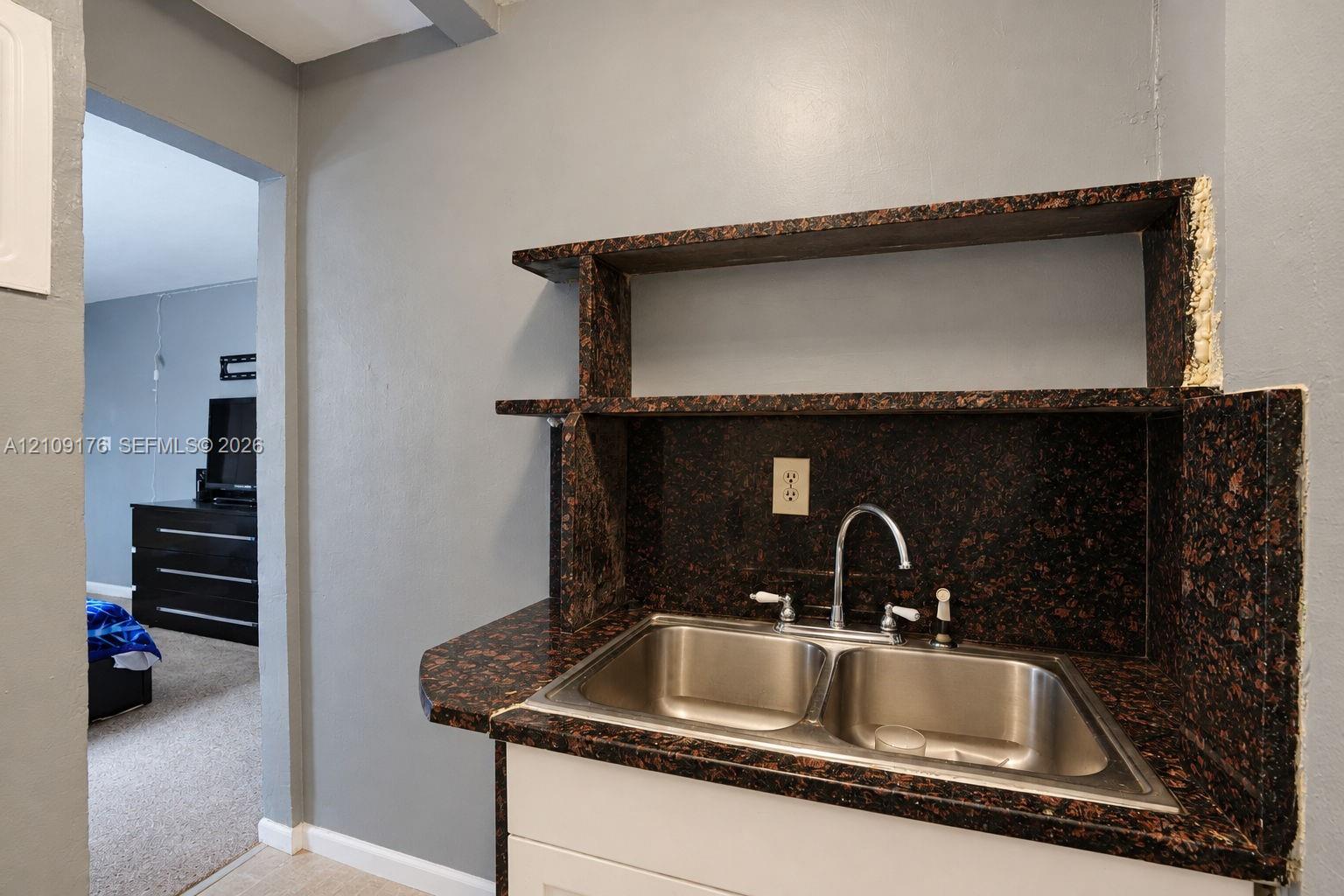 Built-in wet bar featuring stone-finish countertop, dual-basin stainless steel sink, chrome faucet, and integrated shelving