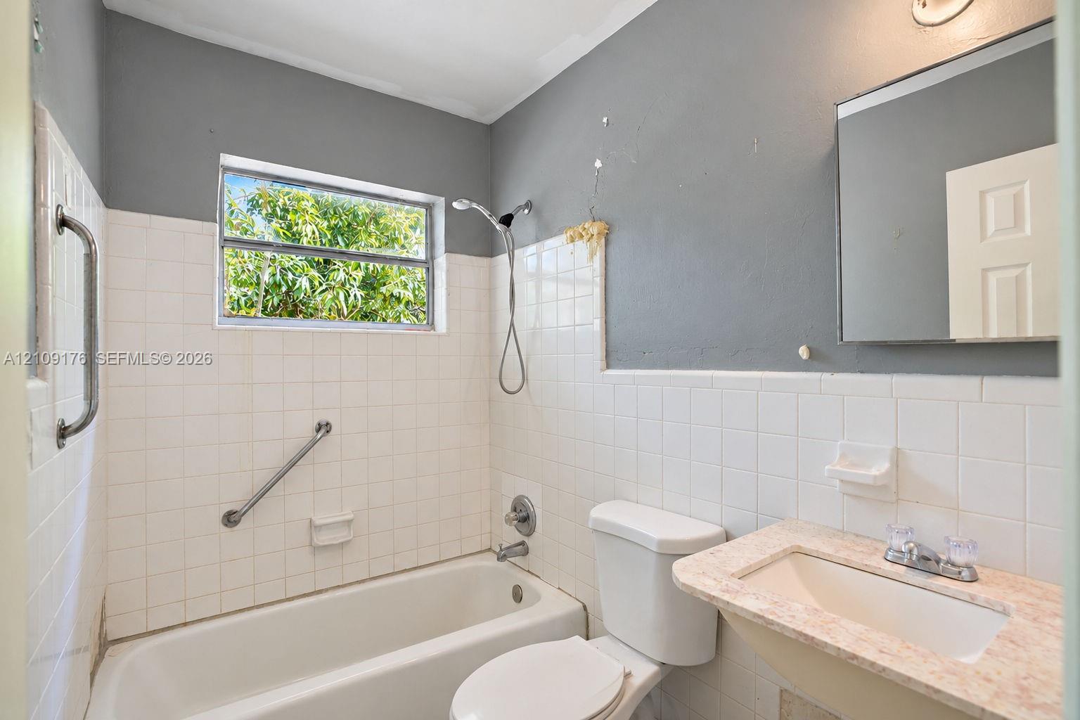 Bathroom featuring a wall-mounted sink with an integrated countertop, square tile tub surround, handheld shower fixture, and a wall-mounted mirror