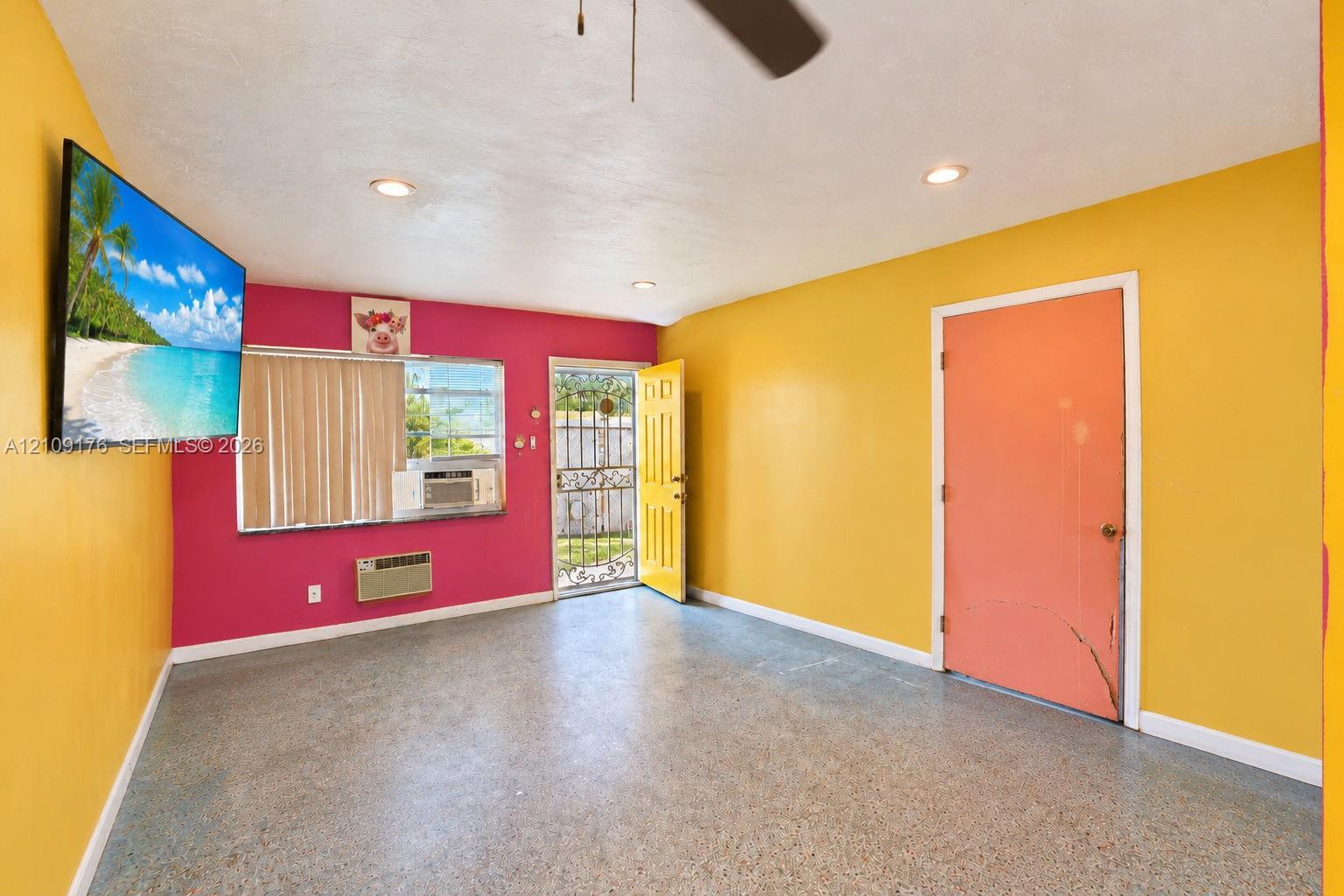 Interior space featuring speckled composite flooring, recessed ceiling lighting, a ceiling fan, a wall-mounted climate control unit, and a metal security door