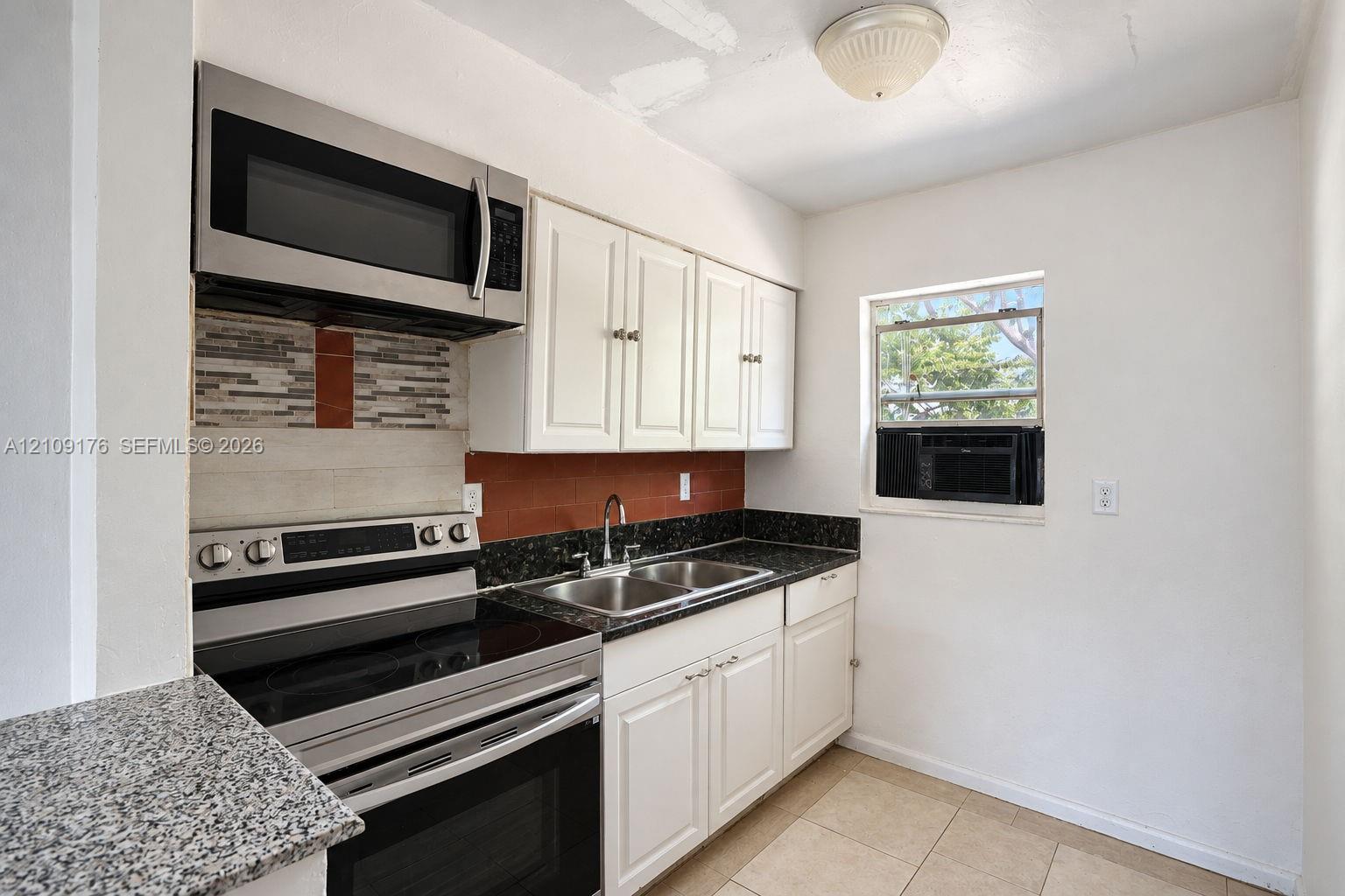 Kitchen featuring stainless steel appliances, over-the-range microwave, white shaker-style cabinetry, dark stone-finish countertops, and tile flooring