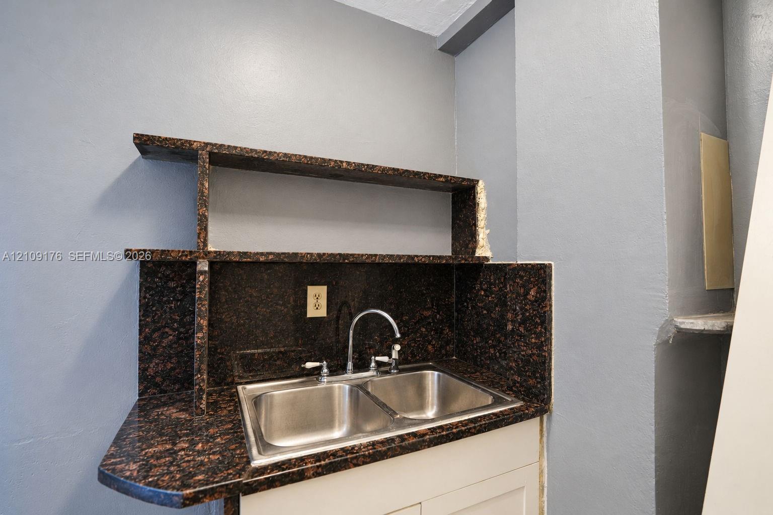 Built-in stone-surface shelving with matching backsplash and dual-basin stainless steel sink featuring a gooseneck faucet