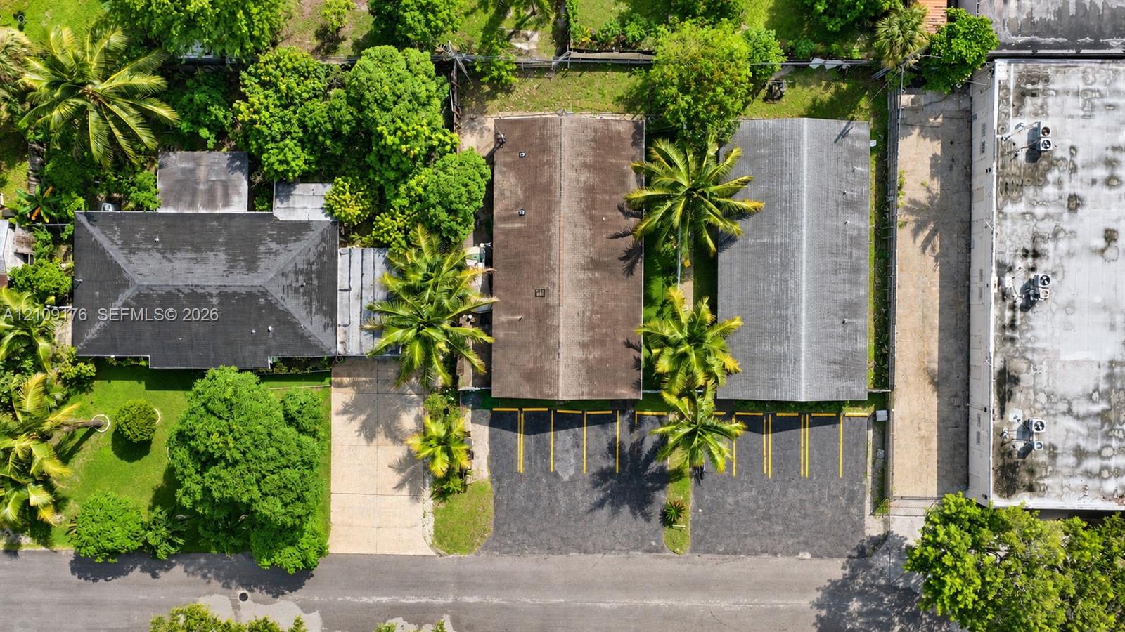 Aerial perspective featuring multiple structures, dedicated paved parking area with striped stalls, and mature trees situated on the property grounds