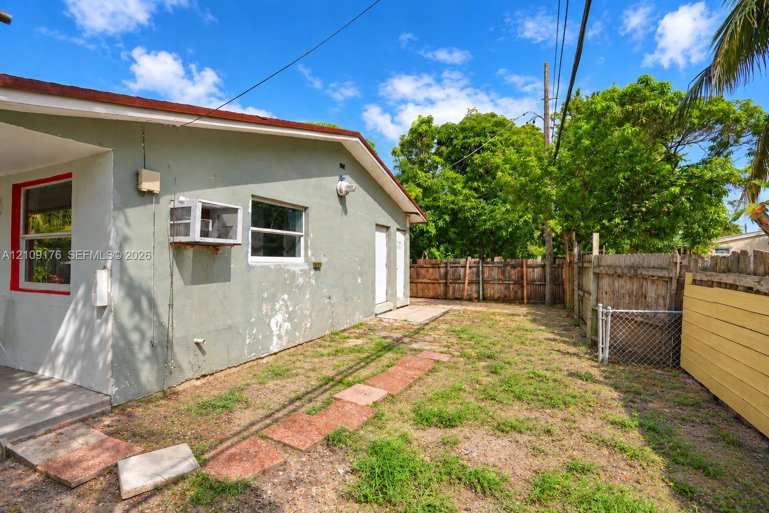 Exterior side yard featuring a concrete pathway, perimeter wood fencing, and mature trees