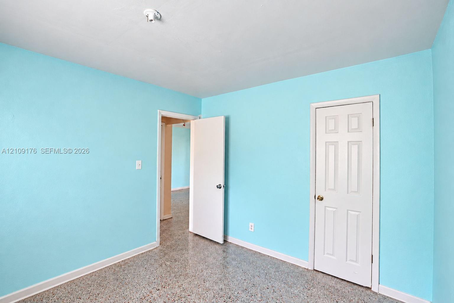 Interior room featuring terrazzo flooring, six-panel interior door, and flush-mount lighting