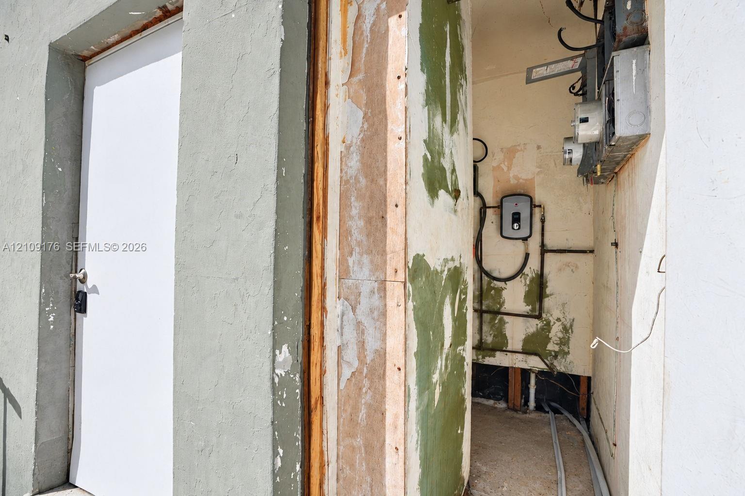 Utility alcove featuring an exterior door, exposed structural framing, wall-mounted electrical panel, and tankless water heater