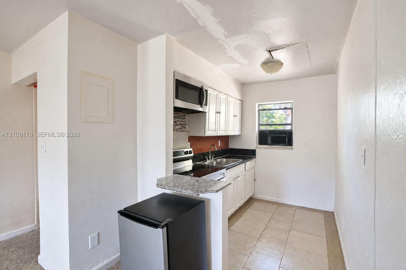 Kitchen featuring white cabinetry, stone-finish countertops, stainless steel microwave, metal sink, and tiled flooring