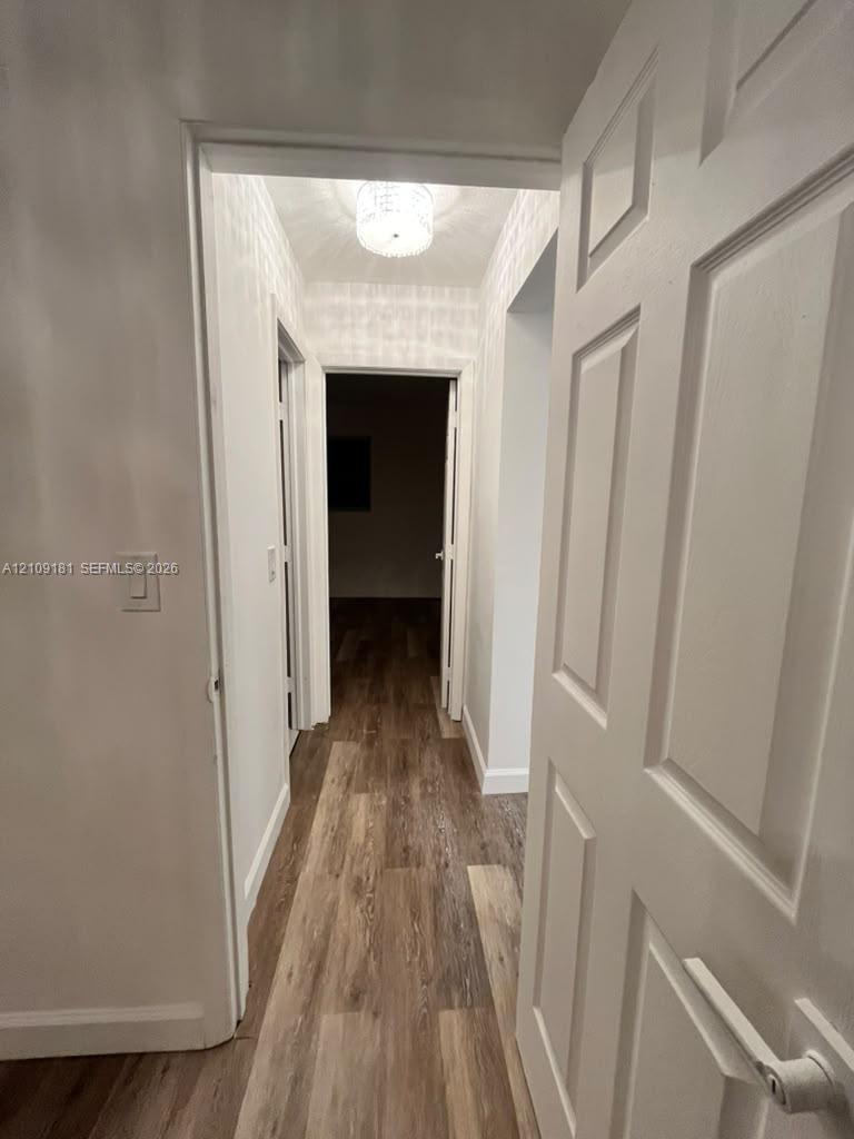 Hallway featuring wood-finish flooring, white multi-panel doors, and a flush-mount drum ceiling light fixture