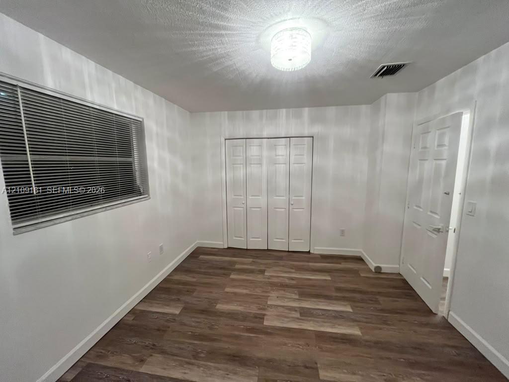 Room featuring wood-finish flooring, white paneled interior doors, a multi-panel closet, and a decorative flush-mount ceiling light fixture