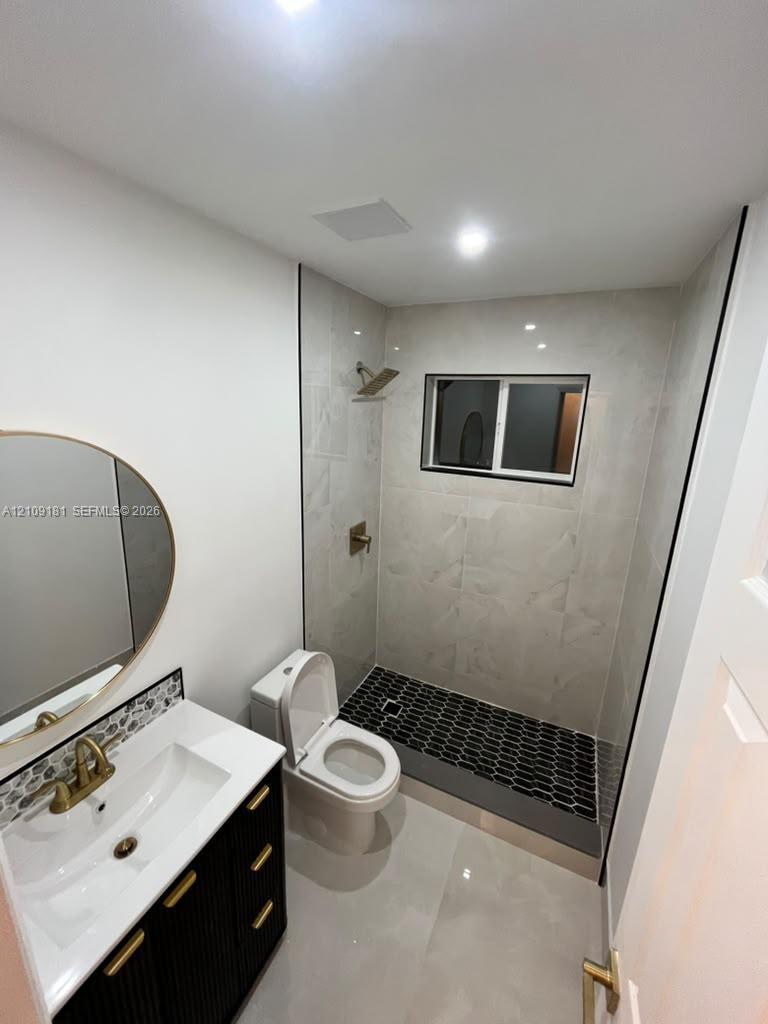 Bathroom featuring a vanity with gold-tone hardware, a tiled walk-in shower with geometric flooring, and a wall-mounted oval mirror
