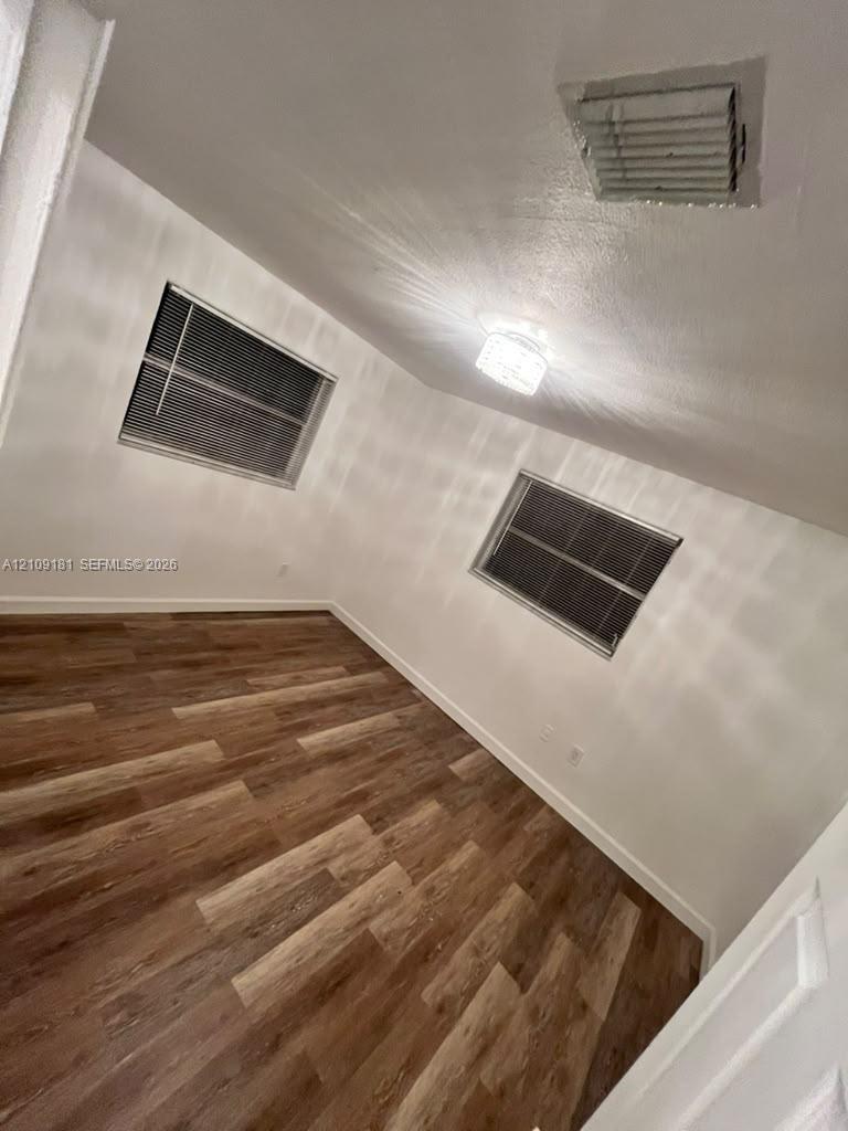Interior room featuring wood-finish flooring, white walls, two windows with horizontal blinds, and a crystal-style flush mount ceiling light