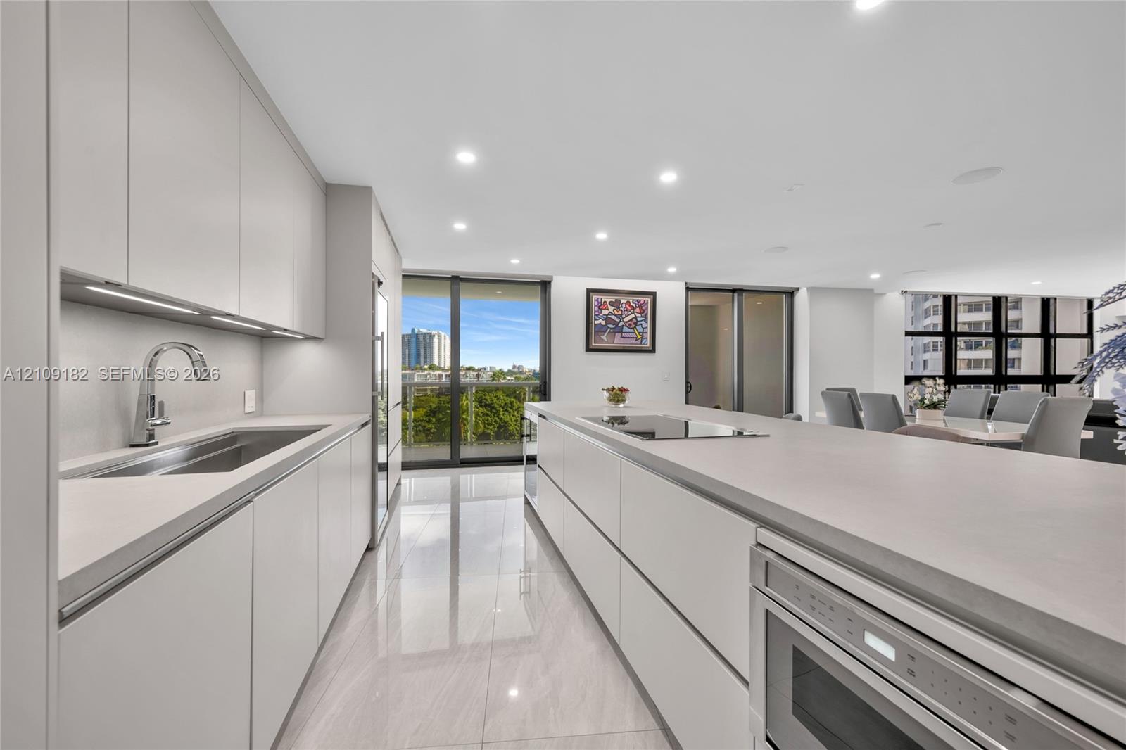 Modern kitchen featuring sleek flat-panel cabinetry, a spacious island with an integrated cooktop, stone-finish countertops, tile flooring, and recessed ceiling lighting