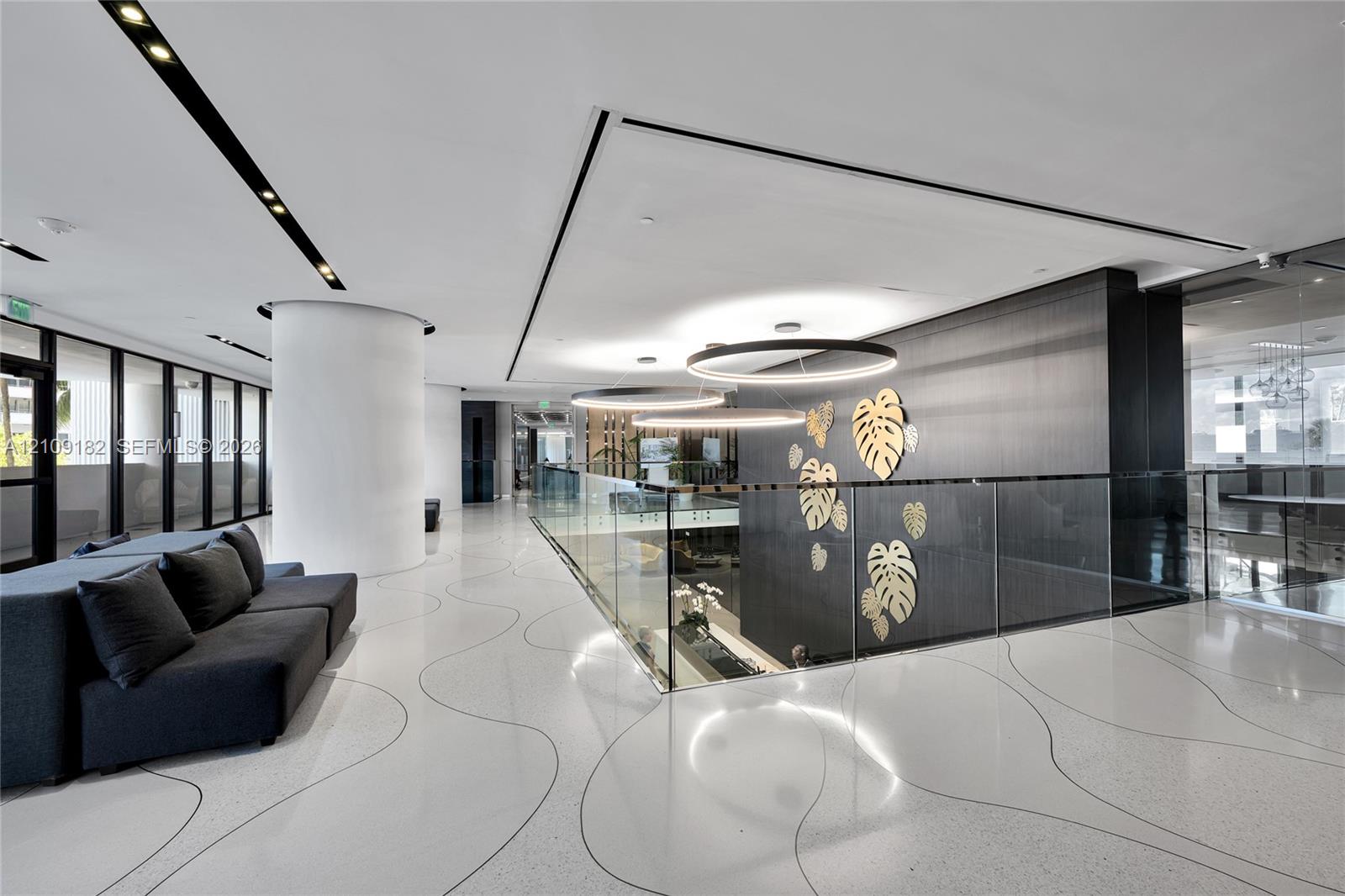 Polished flooring with integrated sweeping line patterns, custom circular overhead lighting, glass panel railing, and a dark accent wall featuring metallic botanical motifs