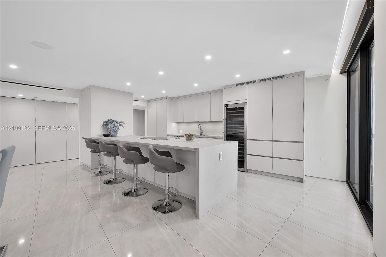 Kitchen featuring a waterfall island with stone countertop, flat-panel cabinetry, integrated wine refrigeration, recessed ceiling lighting, and polished stone flooring