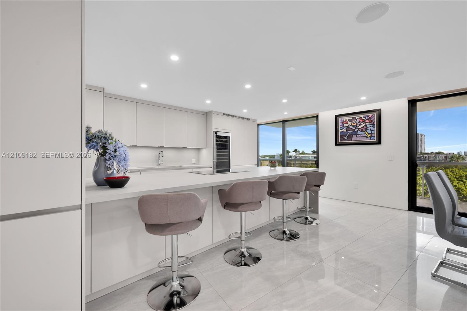 Modern kitchen featuring floor-to-ceiling cabinetry, a sprawling stone-surface island, built-in wine refrigeration, recessed ceiling lighting, and large-format tile flooring