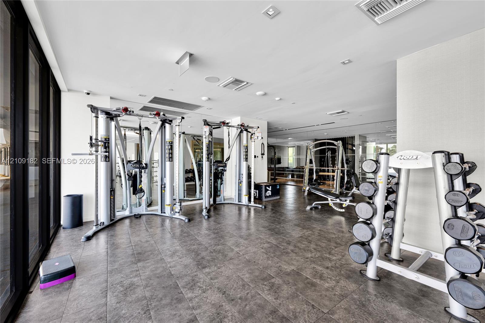 Fitness center featuring large-format tile flooring, recessed ceiling lighting, wall-to-wall mirrors, and floor-to-ceiling windows