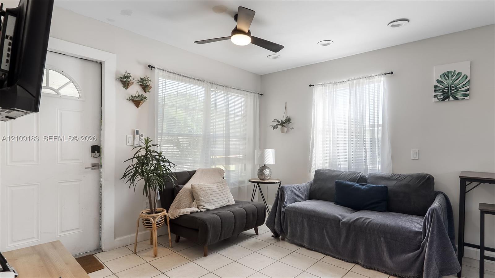 Neutral-toned interior featuring ceramic tile flooring, recessed lighting, a modern ceiling fan with integrated light, and large windows with natural light exposure