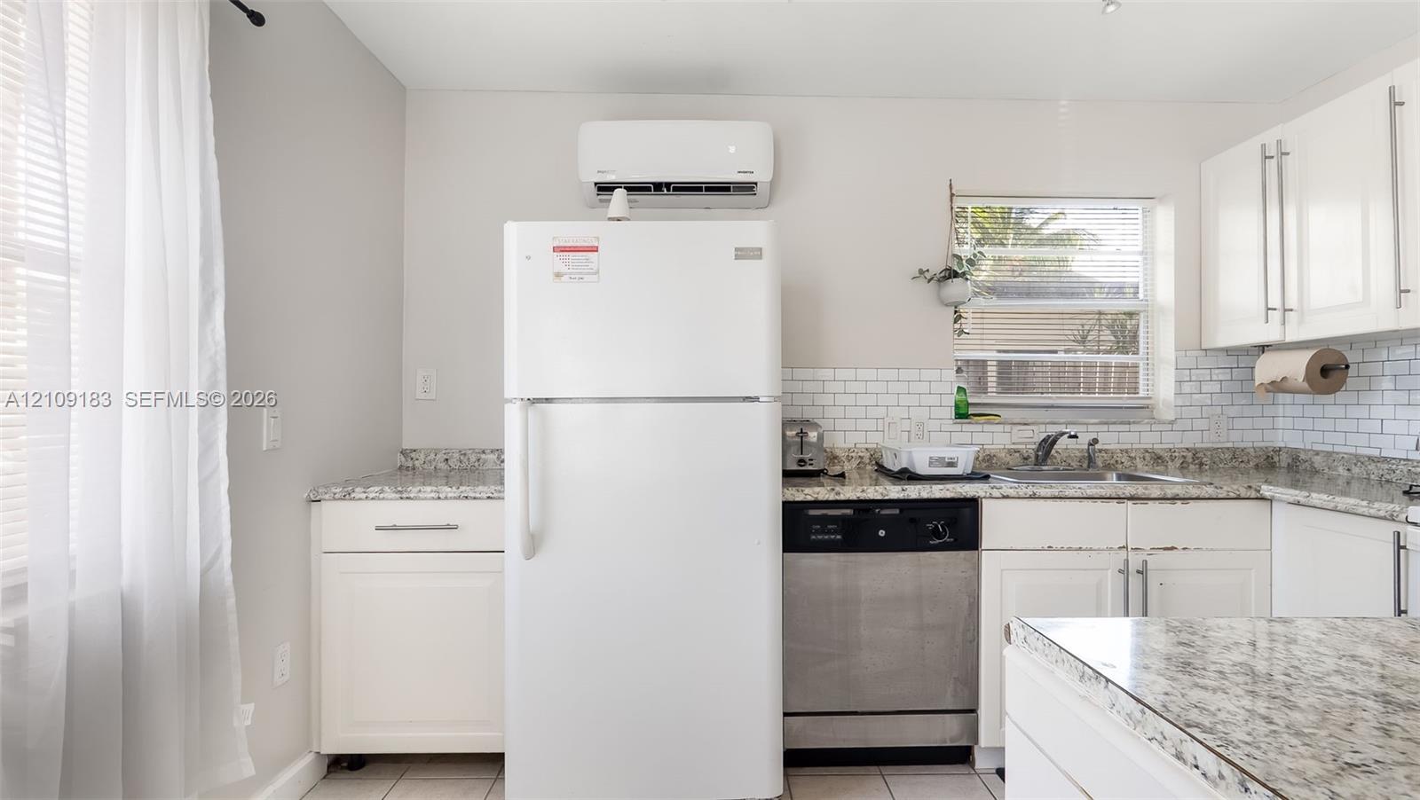Kitchen featuring white shaker-style cabinetry, stone-finish countertops, subway tile backsplash, stainless steel dishwasher, and wall-mounted climate control unit