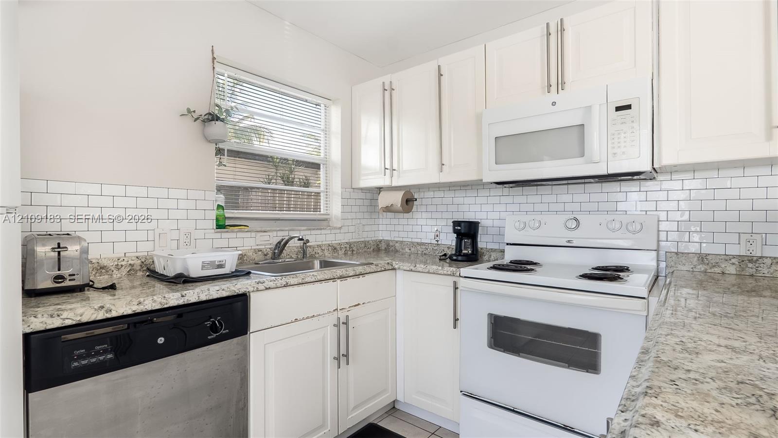 Kitchen featuring white cabinetry, stone-finish countertops, subway tile backsplash, and stainless steel and white appliances