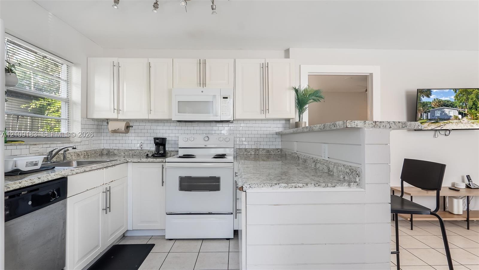 Kitchen featuring white shaker-style cabinetry, stone-finish countertops, subway tile backsplash, white built-in appliances, and a breakfast bar with shiplap detailing