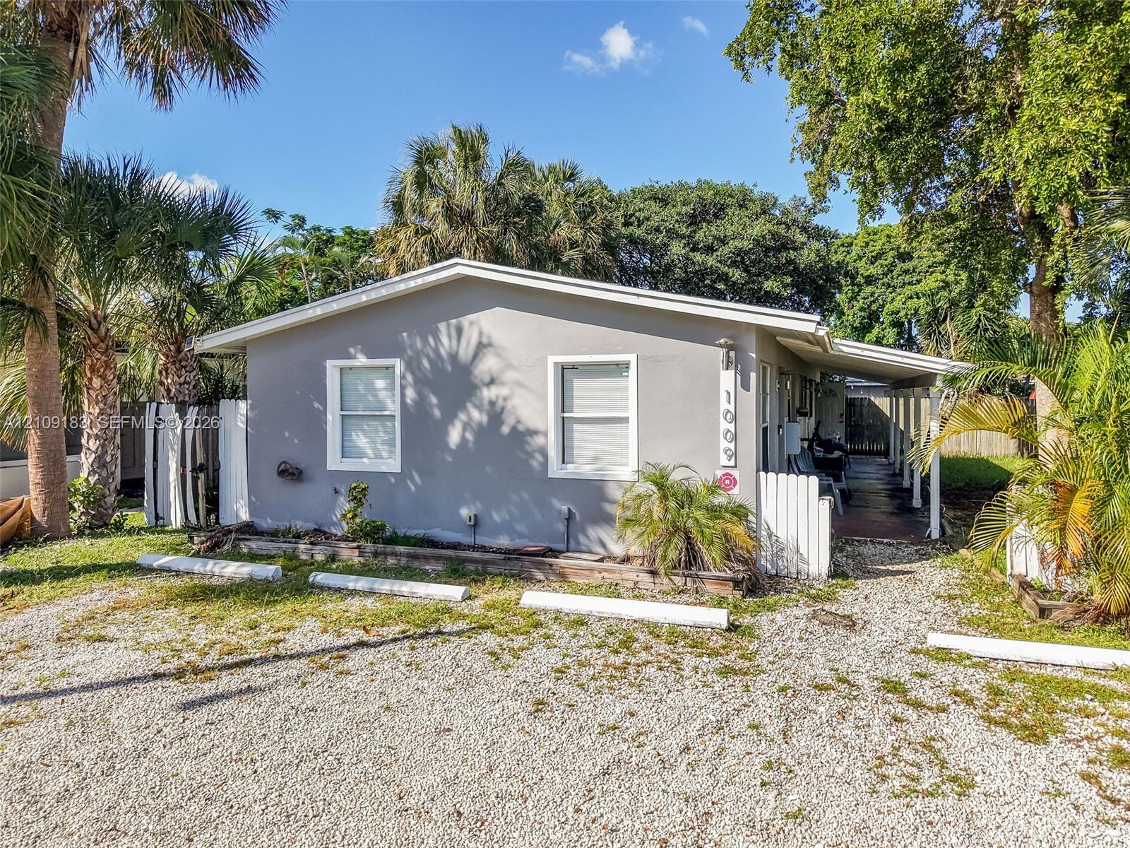 Single-story residence featuring a smooth stucco exterior, dual-pane windows, a covered side porch, and mature palm landscaping