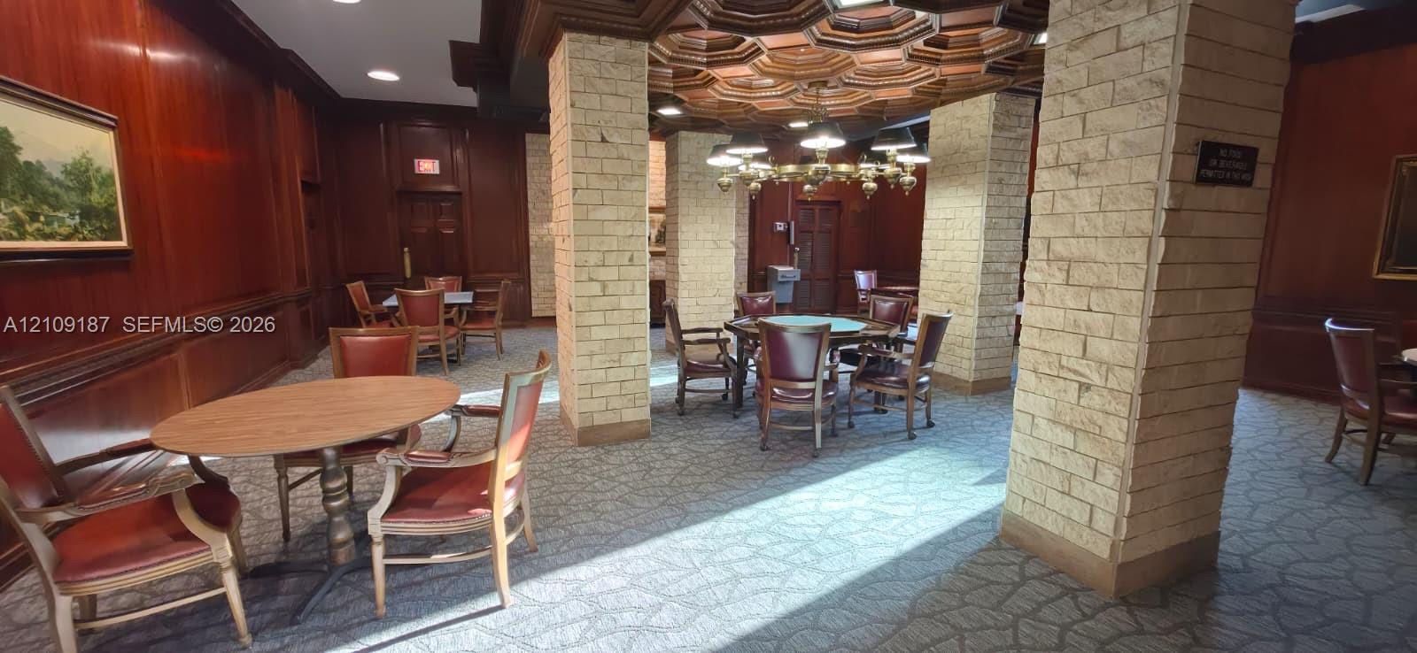 Men's playroom featuring wood-paneled walls, structural columns finished in textured stone, coffered ceiling, and a multi-tiered metal chandelier