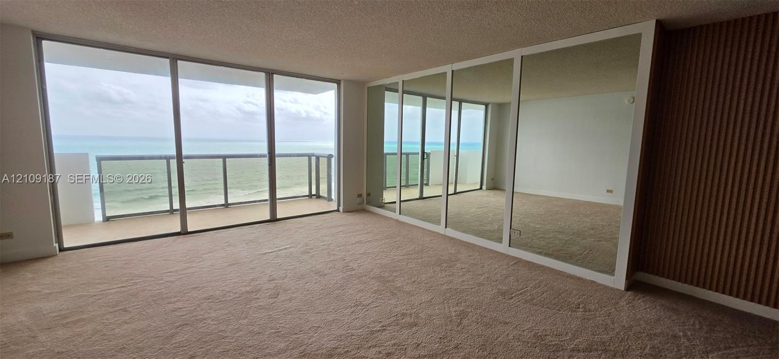 Open-concept space featuring floor-to-ceiling windows, mirrored wall panels to enhance panoramic ocean view, and wood-slat accent wall detailing Open-concept space featuring floor-to-ceiling windows, mirrored wall panels to enhance panoramic ocean view, and wood-slat accent wall detailing