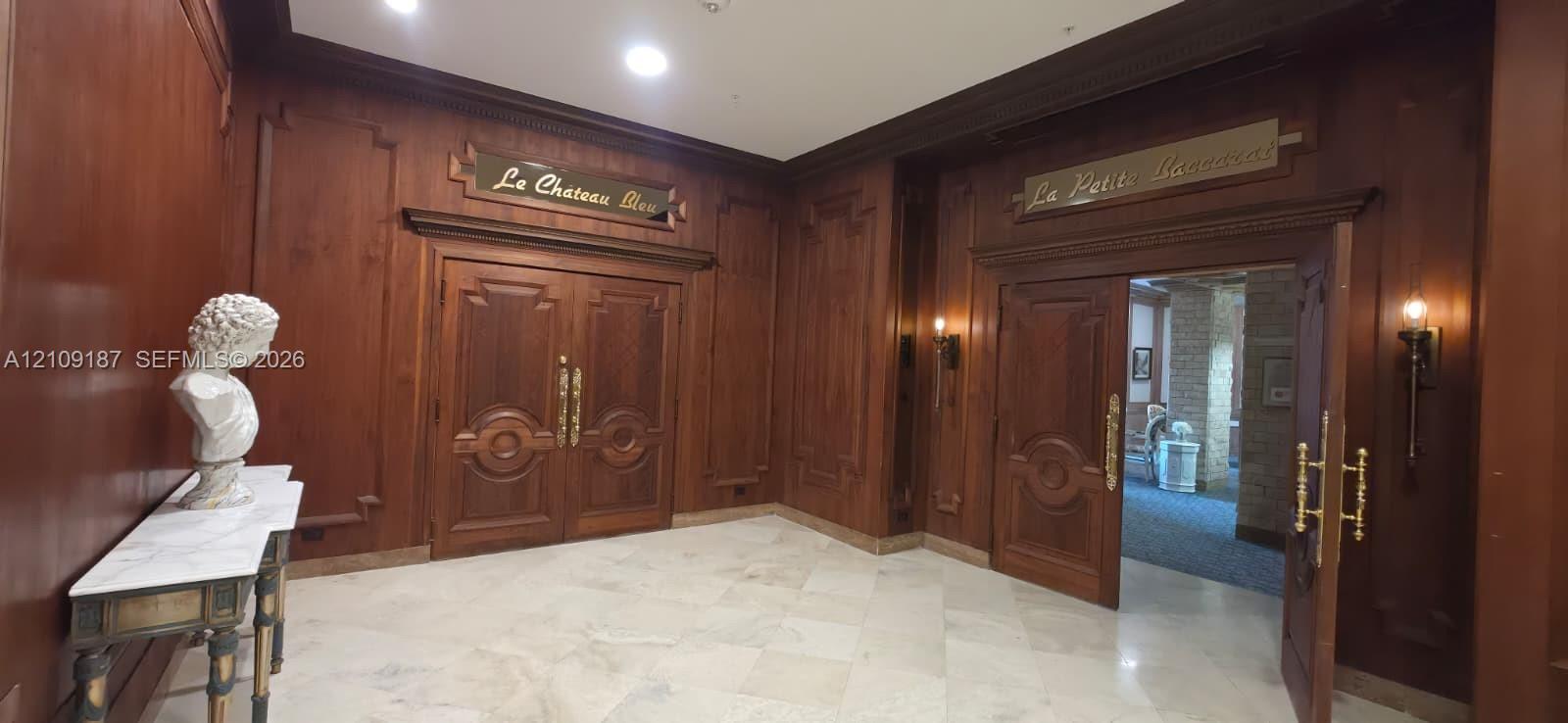 Elegant great room Featuring wood-paneled walls, intricate double wooden doors, marble flooring, and wall-mounted brass light fixtures.