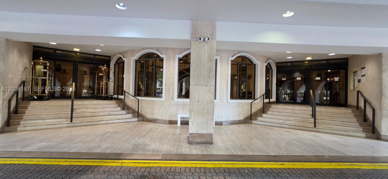 Building covered main entrance and valet parking, featuring marble facade, arched windows, dual staircases with metal handrails, and multi-pane glass entry doors